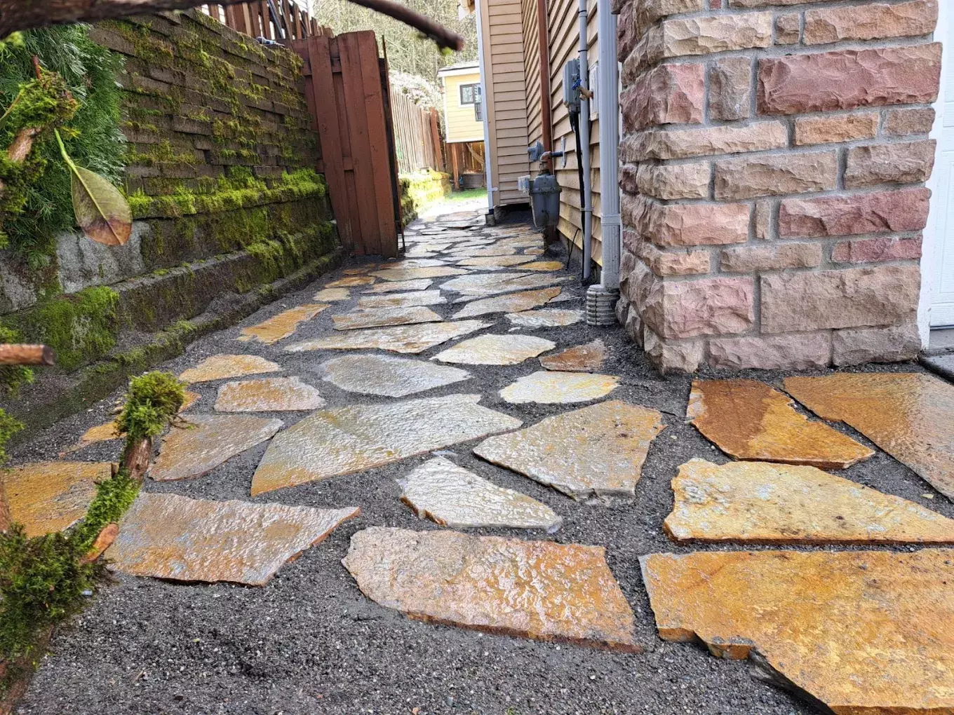 Stone walkway installed along the side of a house with mossy retaining wall.