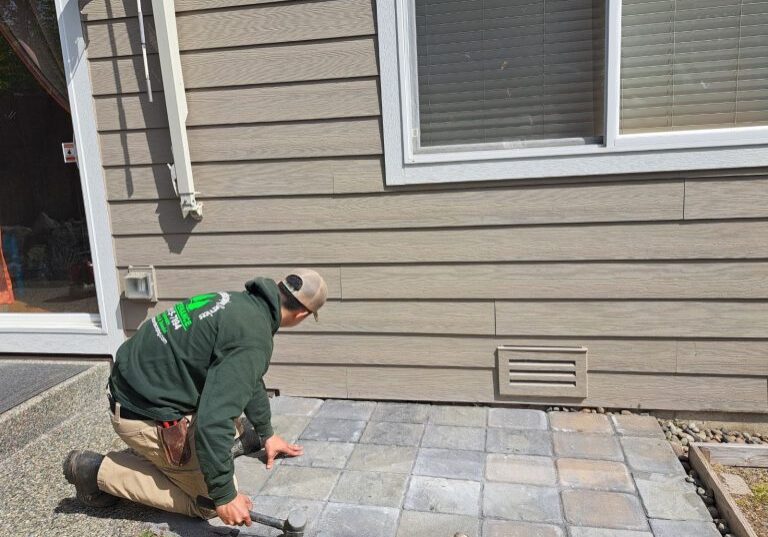 A worker installs concrete pavers outside a house.