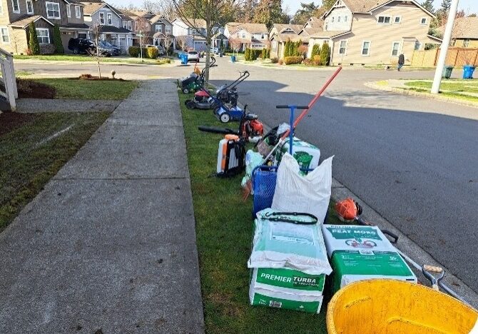 Lawn care and landscaping tools and materials lined up on a residential sidewalk.